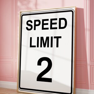 May include: A white sign with black text that reads "SPEED LIMIT 2" in a gold frame.