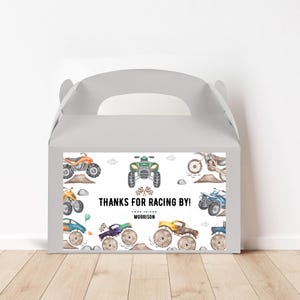 Könnte beinhalten: Eine weiße Geschenkbox mit einem bunten Etikett, auf dem verschiedene Comic-Geländewagen abgebildet sind. Das Etikett lautet "Danke fürs Mitmachen! Dein Freund Morrison".