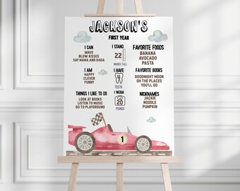 May include: A pink and white illustrated poster with a red race car. The poster is titled "Jackson's First Year" and includes details about Jackson's first year of life, including his height, weight, favorite foods, books, and nicknames.