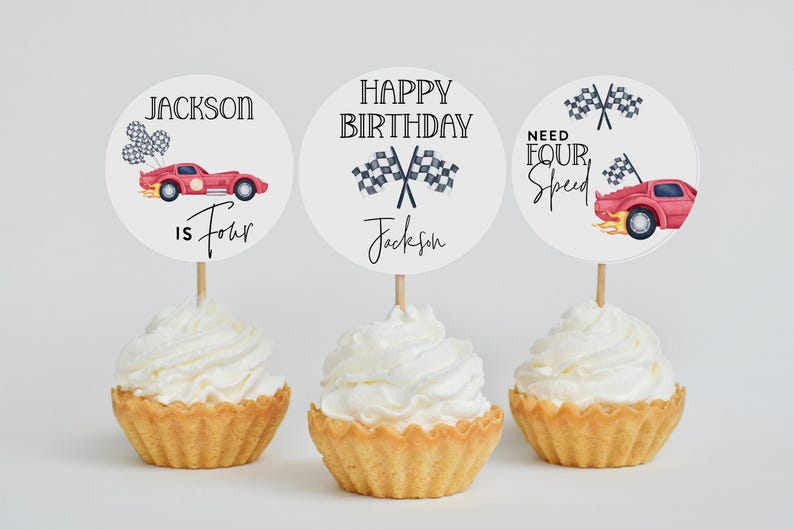 Pu&ograve; includere: Tre cupcake con glassa bianca, ciascuno sormontato da una decorazione di carta rotonda. Le decorazioni presentano grafiche di auto da corsa e il testo "Jackson is Four", "Happy Birthday Jackson" e "Need Four Speed".