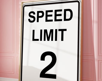 Puede incluir: Arte mural enmarcado con un letrero blanco con texto negro que dice "SPEED LIMIT 2". El letrero tiene un borde negro y un marco dorado. La obra de arte está apoyada contra una pared rosa.