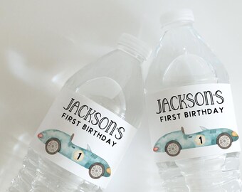 May include: Two clear plastic water bottles with personalized labels for a first birthday party. The labels feature a blue race car with the text "Jackson's First Birthday" and the number "1" on the car.