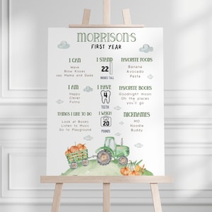 Può includere: Un cartello personalizzato per il primo anno su un cavalletto. Il cartello presenta il nome "Morrison's" e dettagli come altezza (56 cm), peso (9 kg), cibi preferiti, libri e soprannomi. Un trattore e zucche ad acquerello sono in basso.