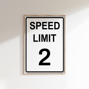 May include: A white speed limit sign with black text and a black border. The sign reads "SPEED LIMIT 2".
