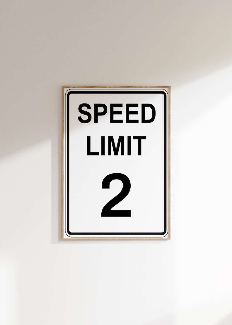 May include: A white speed limit sign with black text and a black border. The sign reads "SPEED LIMIT 2".