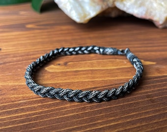 May include: A black and silver braided bracelet with a simple design.