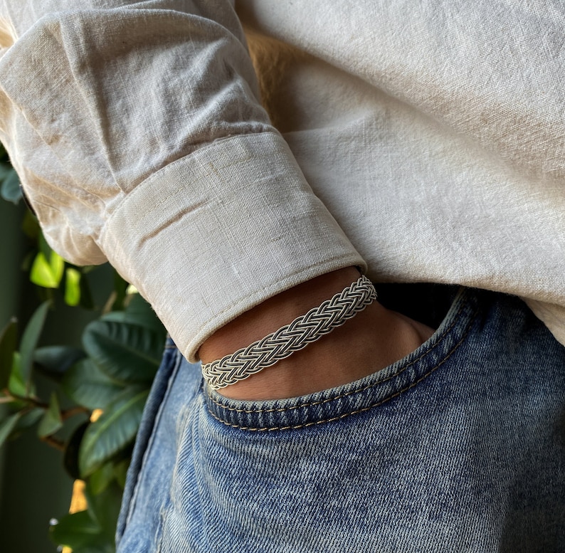 May include: A silver braided bracelet with a woven design. The bracelet is worn on a person's wrist.