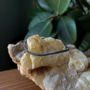 May include: A silver braided chain necklace on a light brown rock.