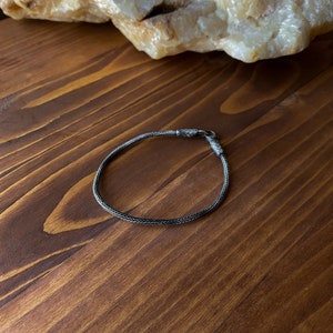 May include: A silver chain bracelet with a clasp closure. The bracelet is on a wooden surface.