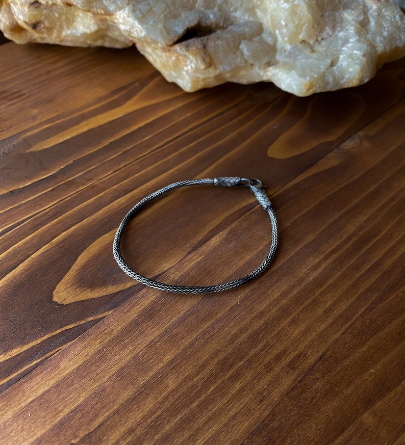 May include: A silver chain bracelet with a clasp closure. The bracelet is on a wooden surface.