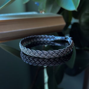 May include: A braided black and silver bracelet with a woven design.