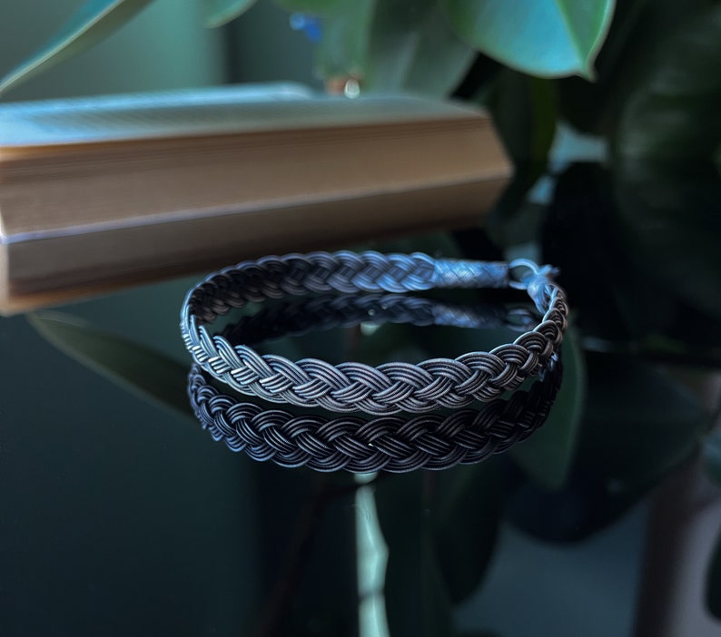 May include: A braided black and silver bracelet with a woven design.