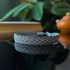 Op de afbeelding: Een zilveren gevlochten armband met een geweven ontwerp. De armband is gemaakt van twee verschillende tinten zilver, waardoor een contrast effect ontstaat.