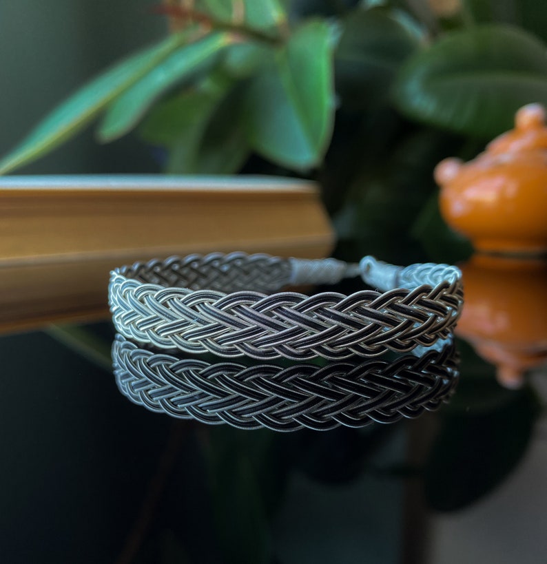 Op de afbeelding: Een zilveren gevlochten armband met een geweven ontwerp. De armband is gemaakt van twee verschillende tinten zilver, waardoor een contrast effect ontstaat.