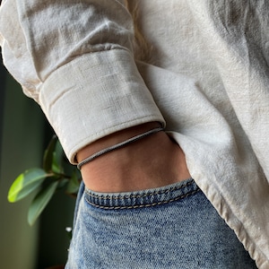 May include: A black braided cord bracelet worn on a person's wrist.