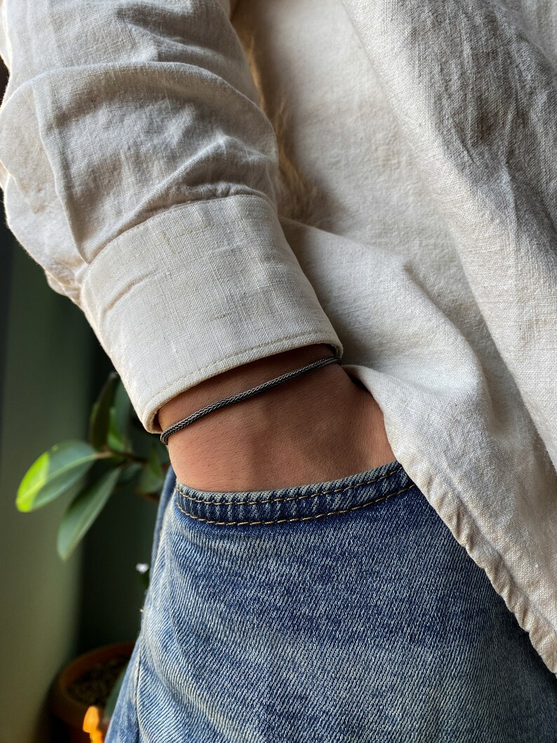 May include: A black braided cord bracelet worn on a person's wrist.