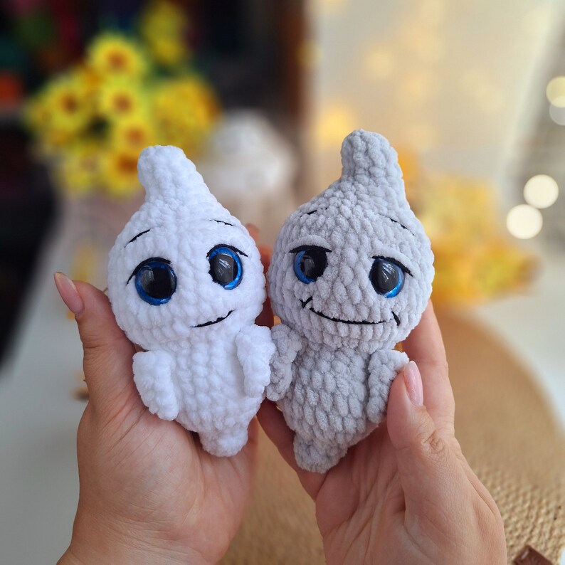May include: Two crocheted ghost plushies with blue eyes. One is white and the other is gray.
