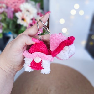 May include: Two pink crocheted gnome keychains with white beards and pink and white hats. The keychains are attached to silver key rings.