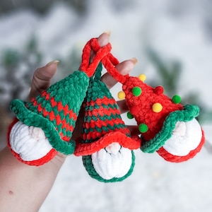 May include: Three crocheted gnome ornaments with red and green hats and white faces. The gnomes are holding hands and have a festive holiday theme.