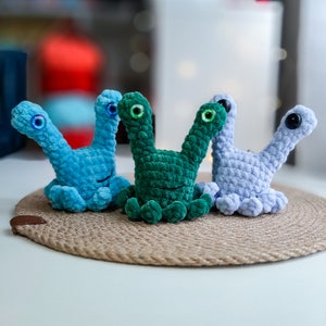 May include: Three crocheted octopus plushies in blue, green, and light blue colors. Each octopus has two large eyes and a smiling mouth.