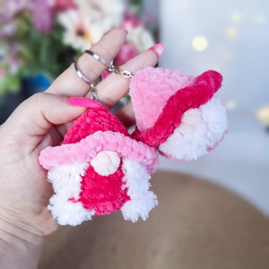 May include: Two pink and white crocheted gnome keyrings with a silver keyring. The gnomes have pink hats and white beards.