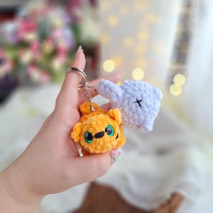 Op de afbeelding: Een sleutelhanger met twee gehaakte dierenbedels. Een bedel is een lichtblauwe olifant met een zwarte X op zijn hoofd. De andere bedel is een gele en oranje tijger met groene ogen.