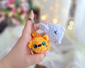 Peut inclure: Un porte-clés avec deux breloques d'animaux en crochet. L'une est un éléphant bleu clair avec un X noir sur la tête. L'autre est un tigre jaune et orange avec des yeux verts.