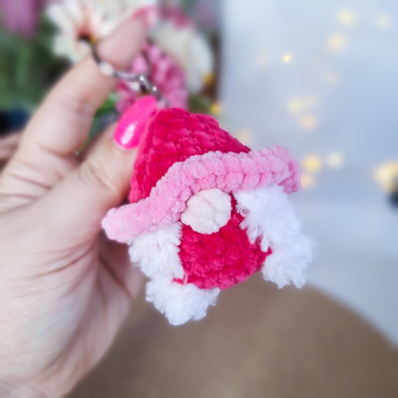 May include: A pink and white crocheted gnome ornament with a white beard and a pink hat.