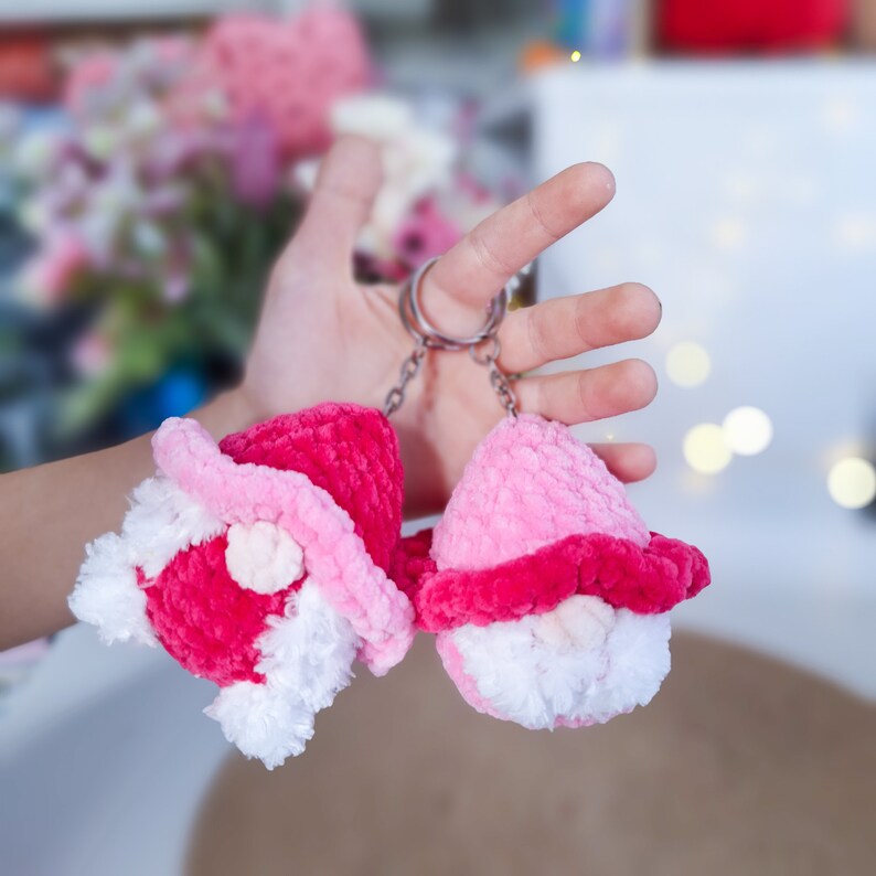 May include: Two pink and white crocheted gnome ornaments with white beards and red hats attached to a silver key chain.
