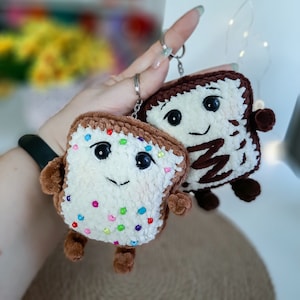 May include: Two crocheted plush toys shaped like food items. One is brown and white and resembles a chocolate bar. The other is white with colorful sprinkles and resembles a cake.
