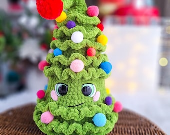 Könnte beinhalten: Ein grüner gehäkelter Weihnachtsbaum mit einem lächelnden Gesicht, verziert mit bunten Pompons und weißen Perlen.
