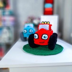 Può includere: Un giocattolo di camion mostro rosso all'uncinetto con ruote nere e occhi blu. Il camion è seduto su un tappetino verde all'uncinetto.