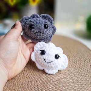May include: Two crocheted cloud-shaped plushies, one gray and one white, with embroidered eyes and smiling mouths.
