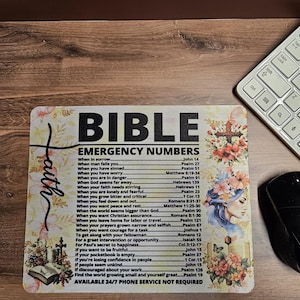 May include: A rectangular Bible emergency numbers mousepad with floral and cross designs. The mousepad features a list of Bible verses for various situations. A keyboard and mouse are visible in the background.