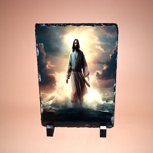 May include: A rectangular slate plaque featuring an image of a figure in a white robe standing in water, with a bright light emanating from behind. The plaque is supported by a black stand.
