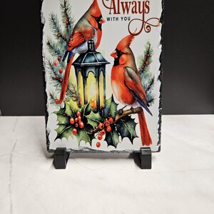 May include: A rectangular slate plaque featuring two red cardinal birds perched near a lantern and holly. The words "I AM Always WITH YOU" are written in a decorative font. The plaque is supported by two black stands.