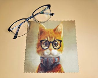 Puede incluir: Un par de gafas de montura oscura con lentes transparentes colocadas junto a un paño de limpieza de microfibra cuadrado con una ilustración impresa de un gato atigrado naranja con gafas de montura negra y una bufanda de punto a rayas.