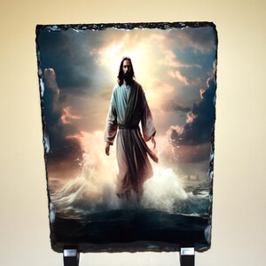 May include: A rectangular stone art piece depicting a figure in flowing robes walking on water. The background features a dramatic sky with clouds and a bright light source. The stone has a rough, dark edge.