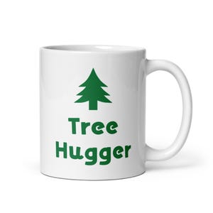 Könnte beinhalten: Weiße Keramiktasse mit einem grünen Baummotiv und dem aufgedruckten Text "Tree Hugger".