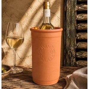 Może przedstawiać: Cylindryczny chłodnik do wina z terakoty z wytłoczonym okrągłym emblematem z napisem WINE COOLER na środku. Naczynie ma pomarańczowo-brązowy kolor i zawiera szklaną butelkę białego wina, ustawioną obok kieliszka do wina na nóżce.