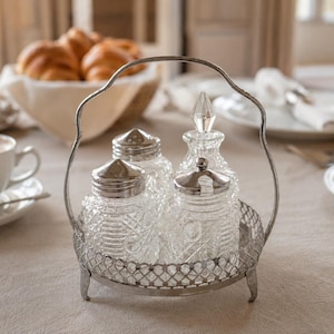 May include: A silver-toned metal caddy with a handle and three feet, containing three clear glass containers with textured patterns and silver-toned metal lids. One container features a pointed glass stopper, while the others have flat lids.