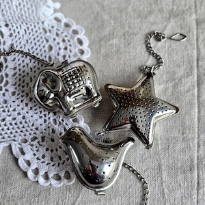 Può includere: Tre infusori per tè in metallo color argento con superfici perforate. Un infusore ha la forma di un elefante con dettagli in rilievo, uno è una stella a cinque punte e uno è un uccellino. Ogni infusore include una catenella in metallo con gancio.