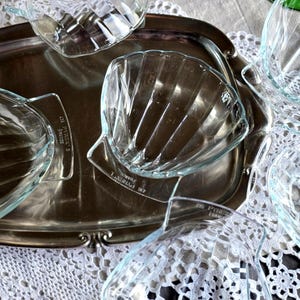 May include: A collection of clear glass shell-shaped serving dishes, some with handles, arranged on a silver serving tray. The dishes are on a white lace tablecloth. The dishes are marked "PYREX" and "FRANCE".