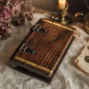 Pode incluir: Uma caixa de madeira castanha escura com detalhes em latão e dobradiças pretas, semelhante a um livro. A imagem apresenta uma vela acesa, flores secas e chaves antigas. A caixa tem formato retangular.