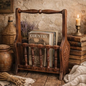 May include: A vintage wooden magazine rack with a handle, filled with books. The rack is dark brown with carved details and a slatted front. The cover of the top magazine reads "COUNTRY". The scene includes a candle, books, and rustic decor.