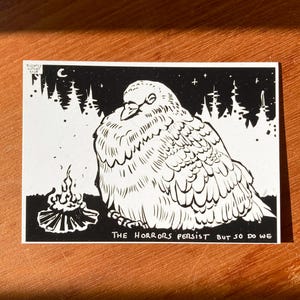 Könnte beinhalten: Schwarz-weiß-Illustration eines Vogels, der vor einem Lagerfeuer mit einem Wald im Hintergrund sitzt. Der Text "THE HORRORS PERSIST BUT SO DO WE" befindet sich unter dem Vogel.