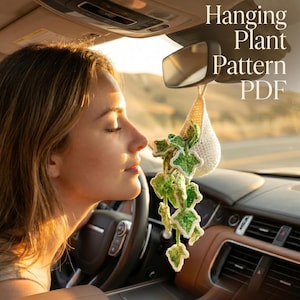 May include: A cream-coloured crocheted hanging plant with green and white leaves hangs from a car's rearview mirror. The image includes text that reads "Crochet Hanging Plant Pattern PDF" and "Add a Soft & Cozy Vibe to Your car."