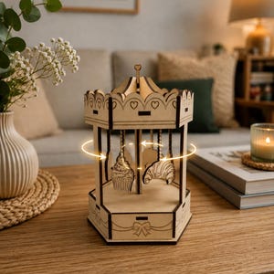 May include: A light-coloured wooden carousel ornament featuring laser-cut designs of a cupcake and a croissant hanging from the canopy. The structure has a scalloped roof with heart cutouts and a bow detail on the base, with a glowing circular arrow.