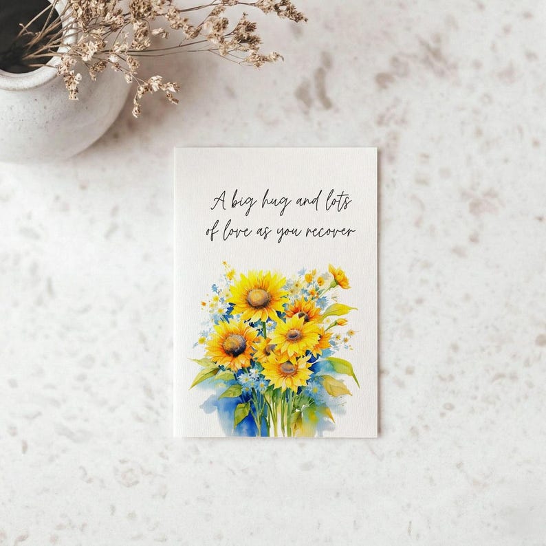A greeting card with a watercolor illustration of yellow sunflowers and blue flowers, accompanied by the text "A big hug and lots of love as you recover"