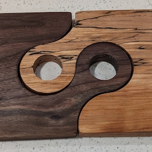 May include: A wooden serving tray with a yin yang design. The tray is made of two different types of wood, one dark and one light. The tray has two cutouts in the shape of circles.